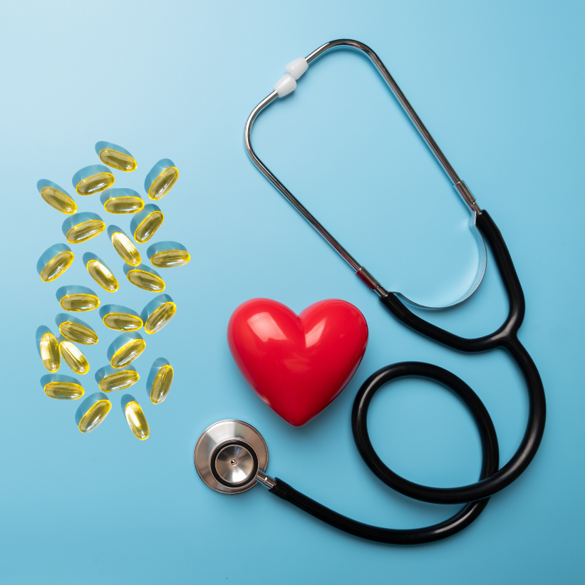 Red heart model, stethoscope, and golden softgel supplements on a light blue background