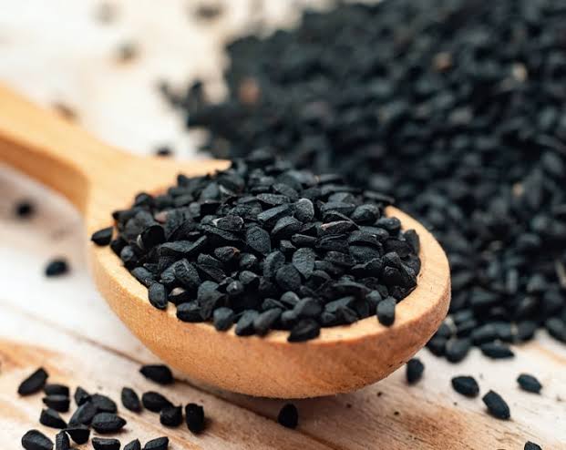 Wooden spoon filled with black cumin seeds on a rustic wooden surface