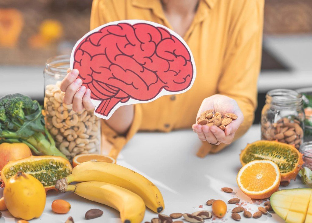 Person holding a brain cutout and almonds with healthy foods on the table