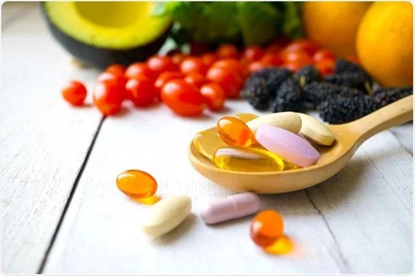 Supplement capsules on a wooden spoon with fresh produce in the background