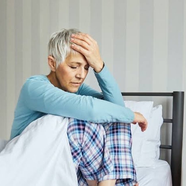 Older woman sitting in bed looking tired after sleep